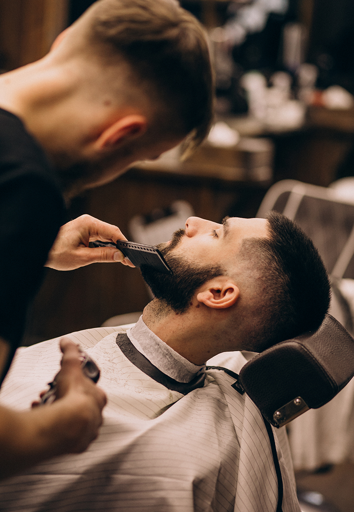 Barber trimming a client's beard with a comb and clippers